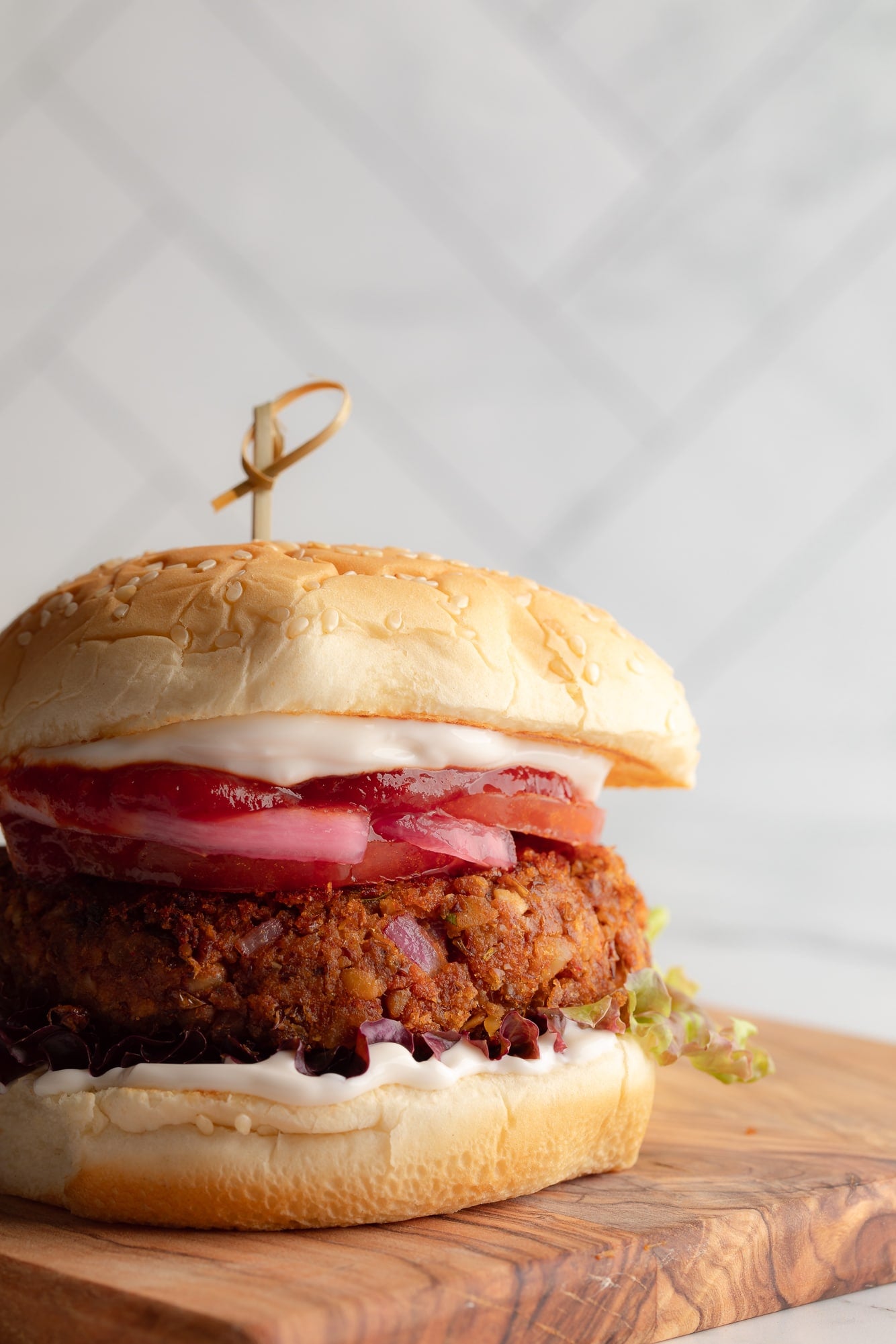 side view of a lentil burger on a bun topped with vegan mayo and ketchup.