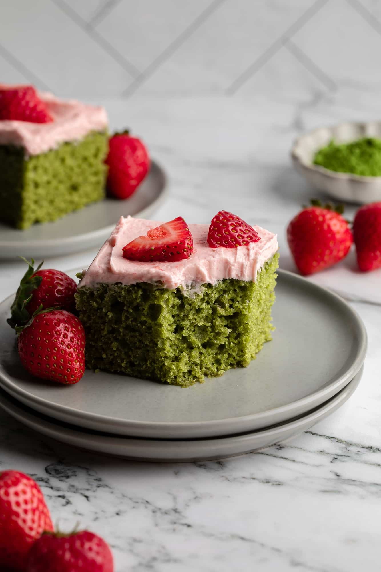 side view of a square slice of vegan strawberry matcha cake with a bite missing on a grey plate.