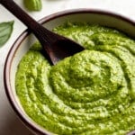 close up on a wooden spoon in a small bowl of vegan pesto.