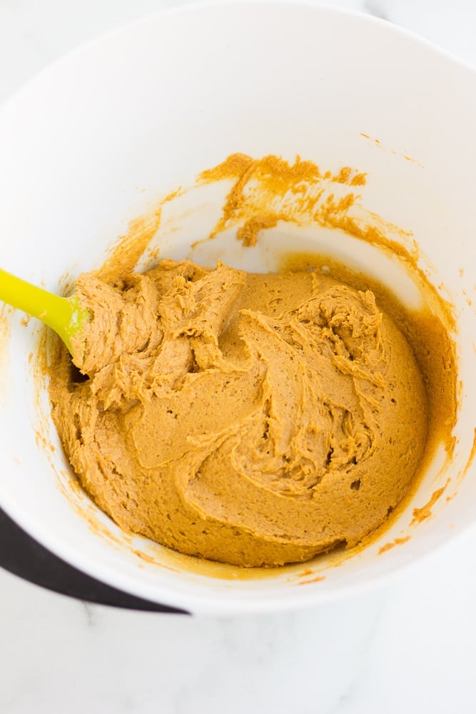 overhead view of a spatula stirring vegan pumpkin cookie dough in a large white bowl.