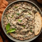 overhead view of a bowl of marry me lentils topped with a slice of bread and basil.