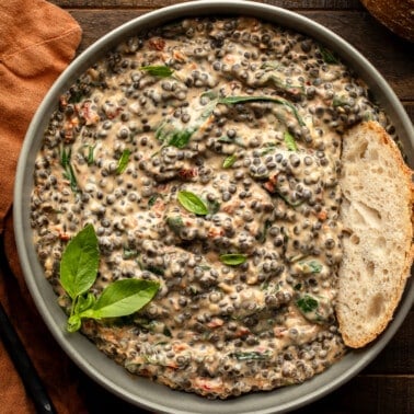 overhead view of a bowl of marry me lentils topped with a slice of bread and basil.