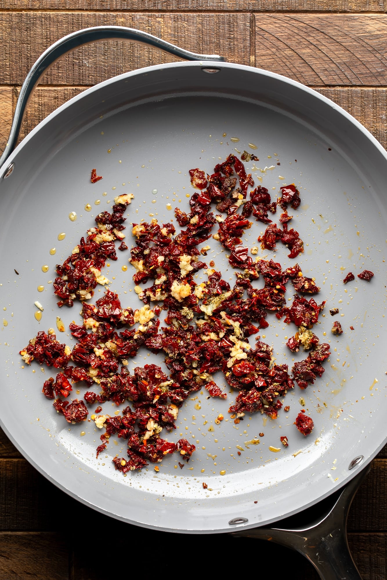 overhead view of sun-dried tomatoes and garlic cooking in a large skillet.