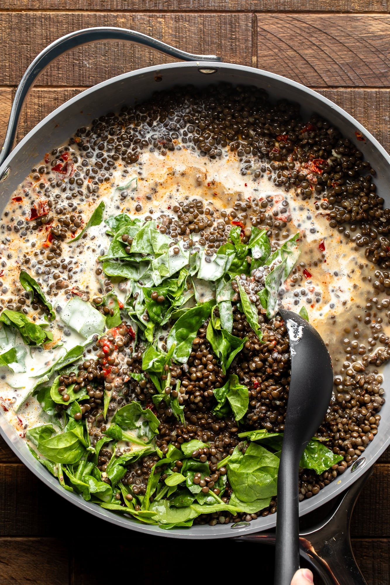overhead view of a black spoon stirring the ingredients for marry me lentils together in a large skillet.
