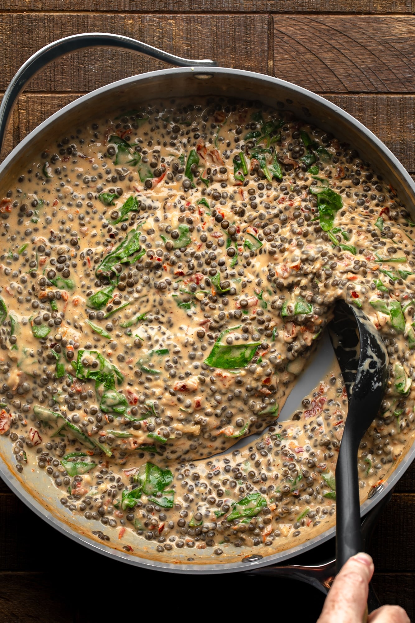 overhead view of a black spoon being dragged through a skillet full of vegan marry me lentils.