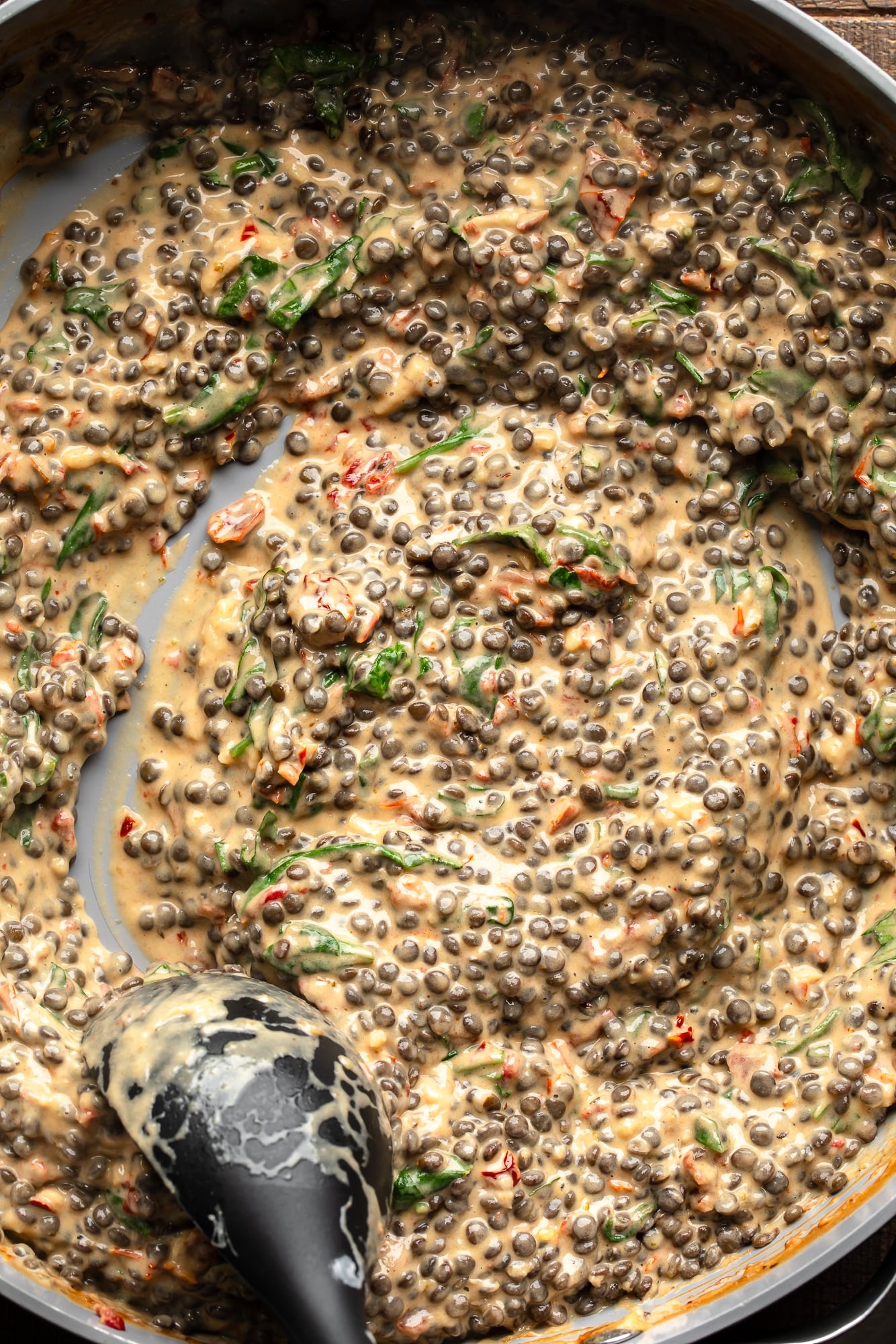 overhead view of a black spoon being dragged through a skillet full of vegan marry me lentils.