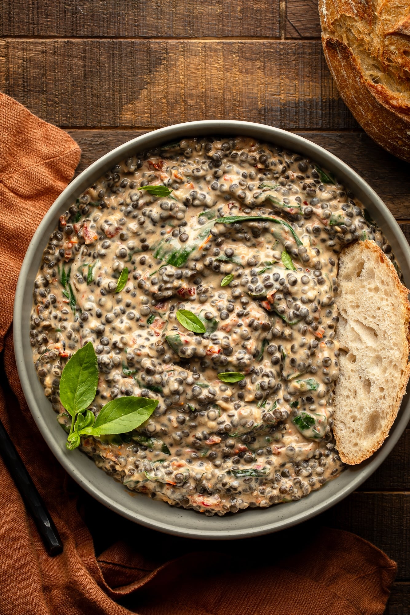 overhead view of a bowl of marry me lentils topped with a slice of bread and basil.