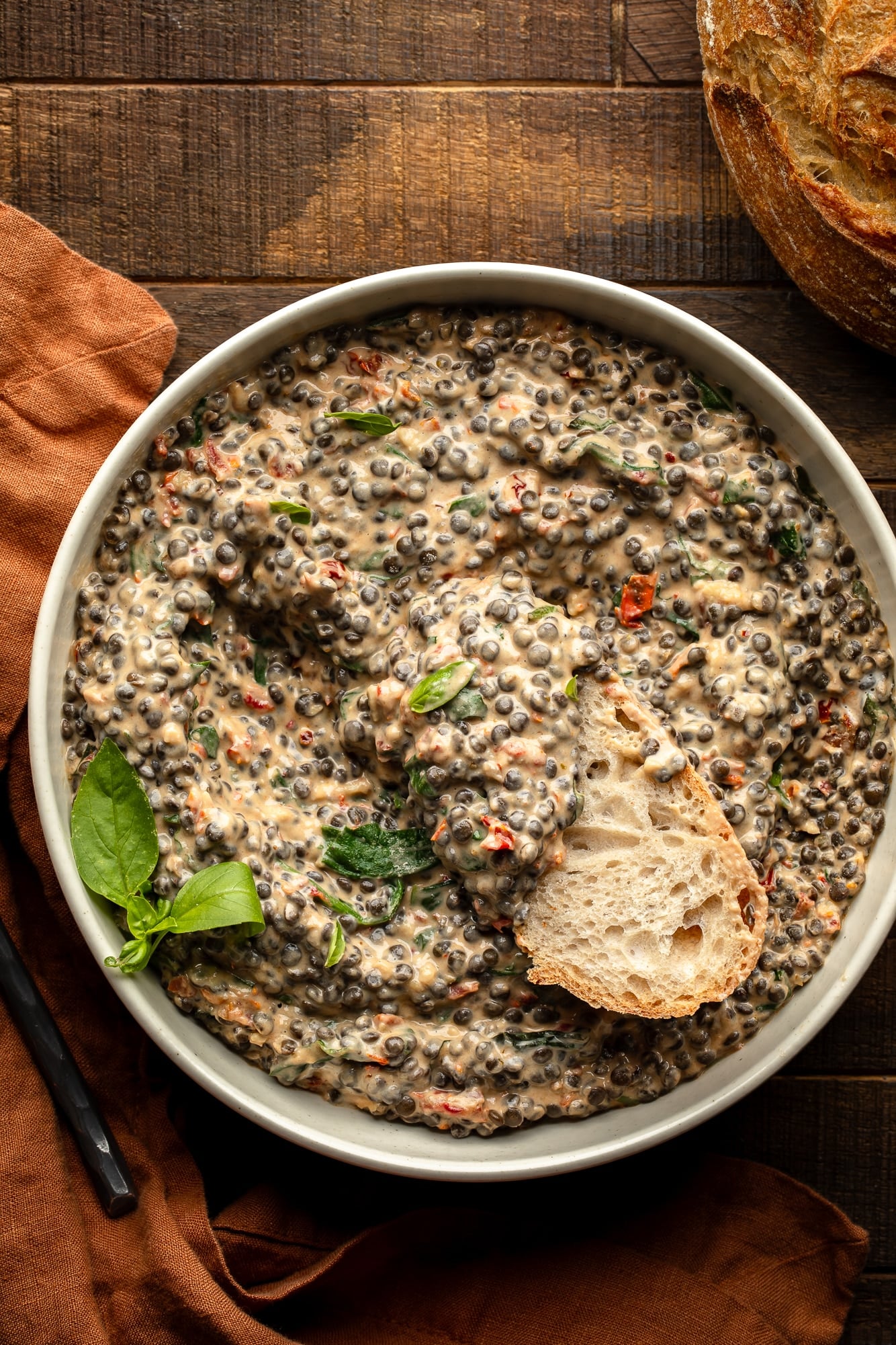 overhead view of a piece of bread being dunked into a bowl of marry me lentils.
