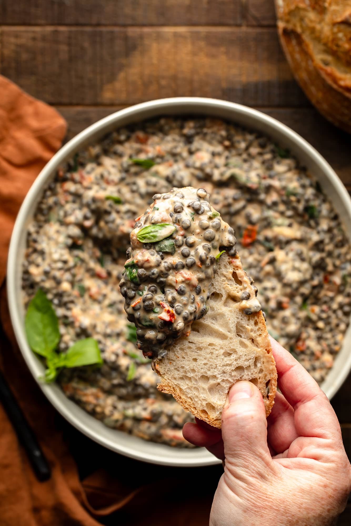 close up of a hand holding a piece of bread with a scoop of marry me lentils.