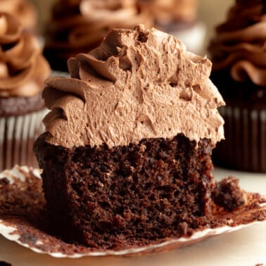 side view of a vegan chocolate cupcake topped with chocolate frosting cut in half.