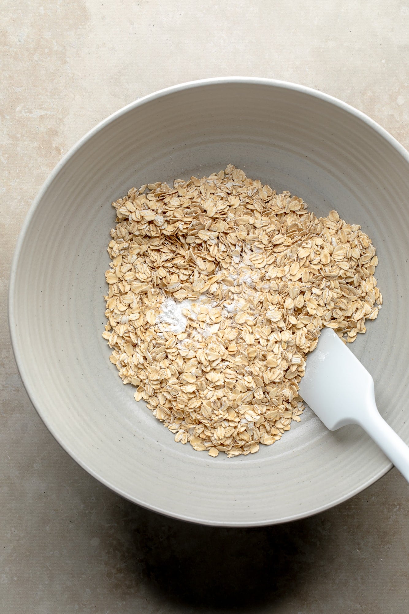 overhead view of rolled oats and a white spatula in a large bowl.