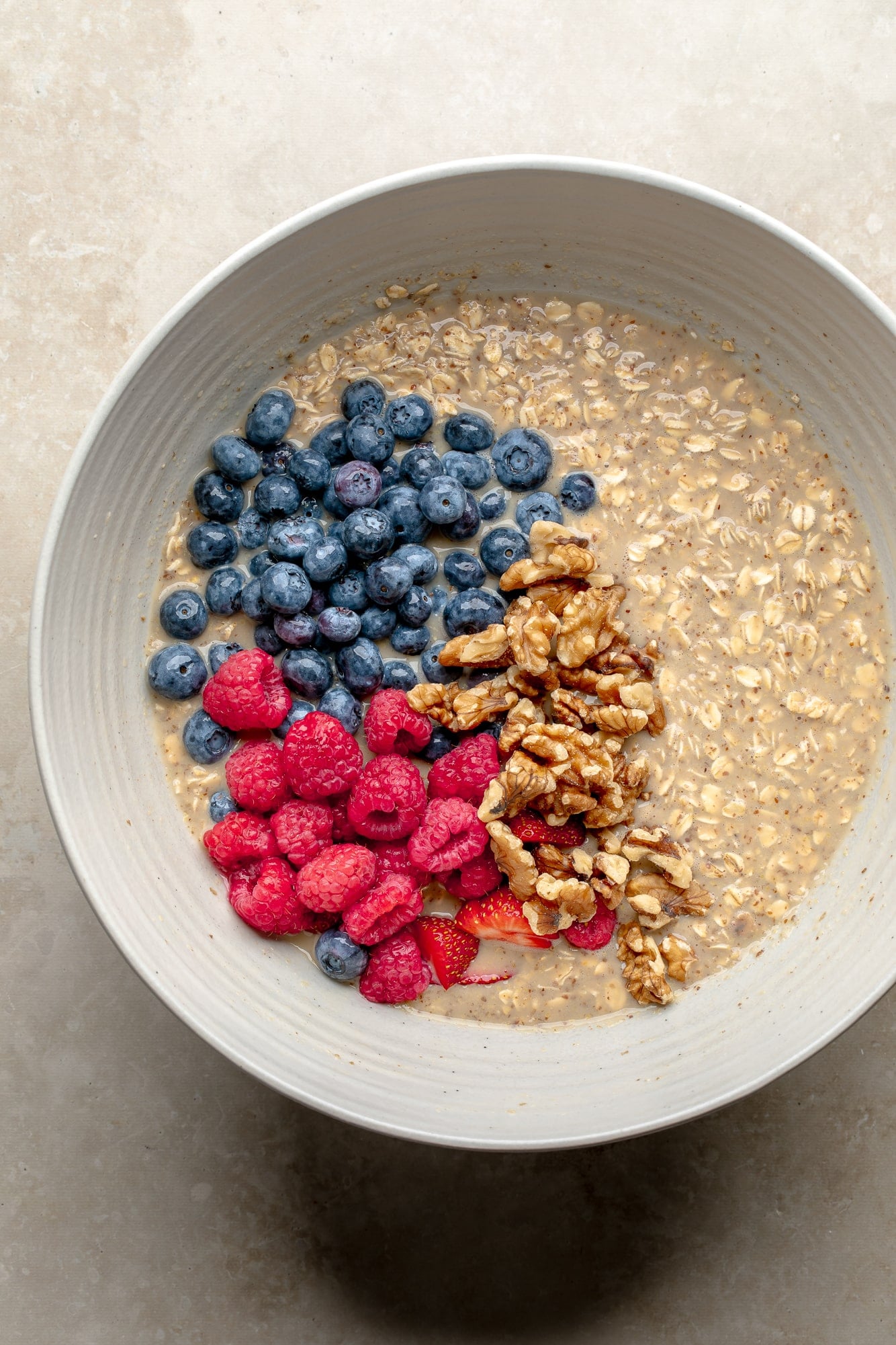 overhead view of fresh berries and walnuts on top of the wet oatmeal mixture for baked berry oatmeal in a large bowl.