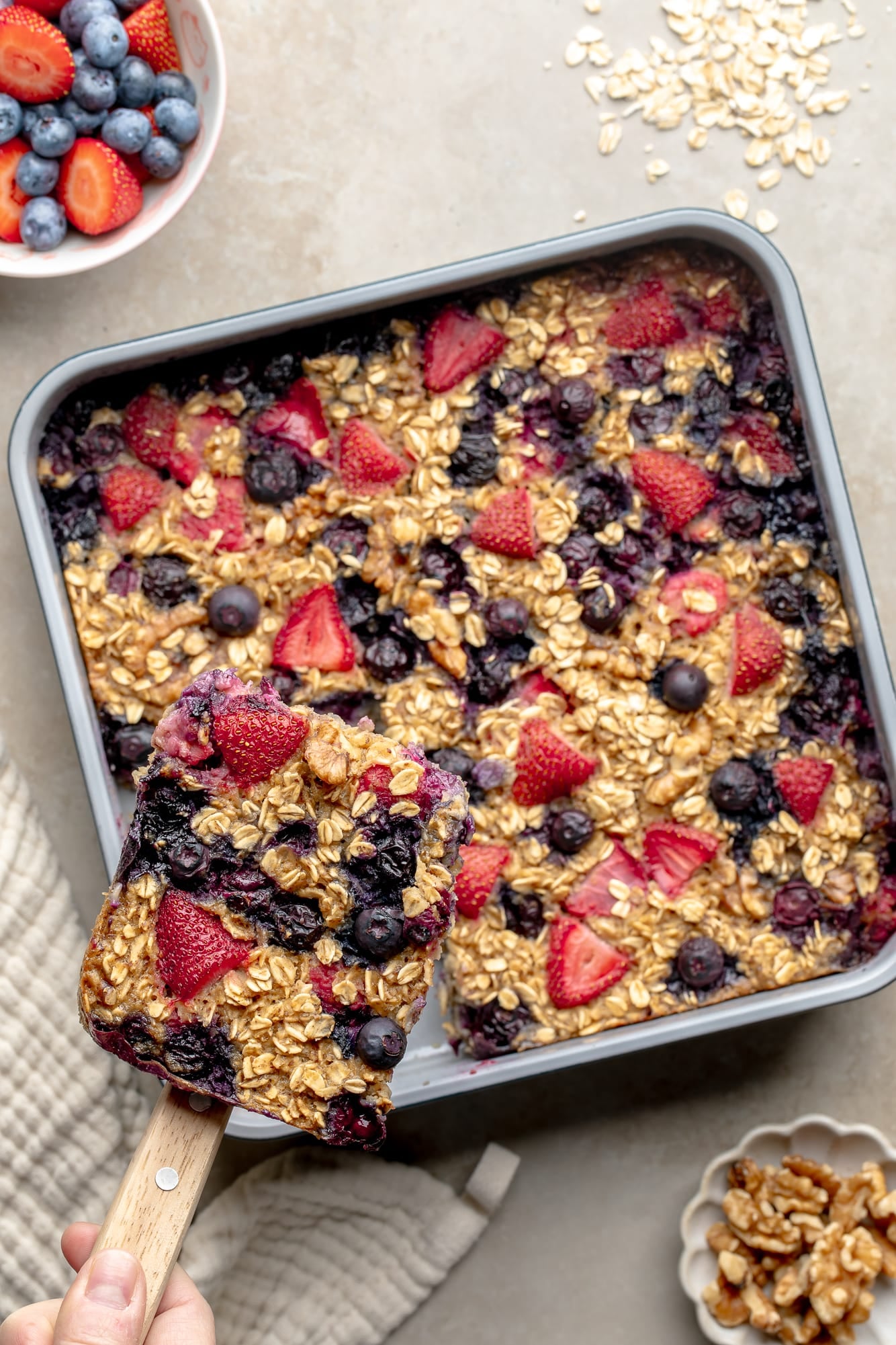 overhead view of a slice of baked berry oatmeal being lifted from the baking pan.