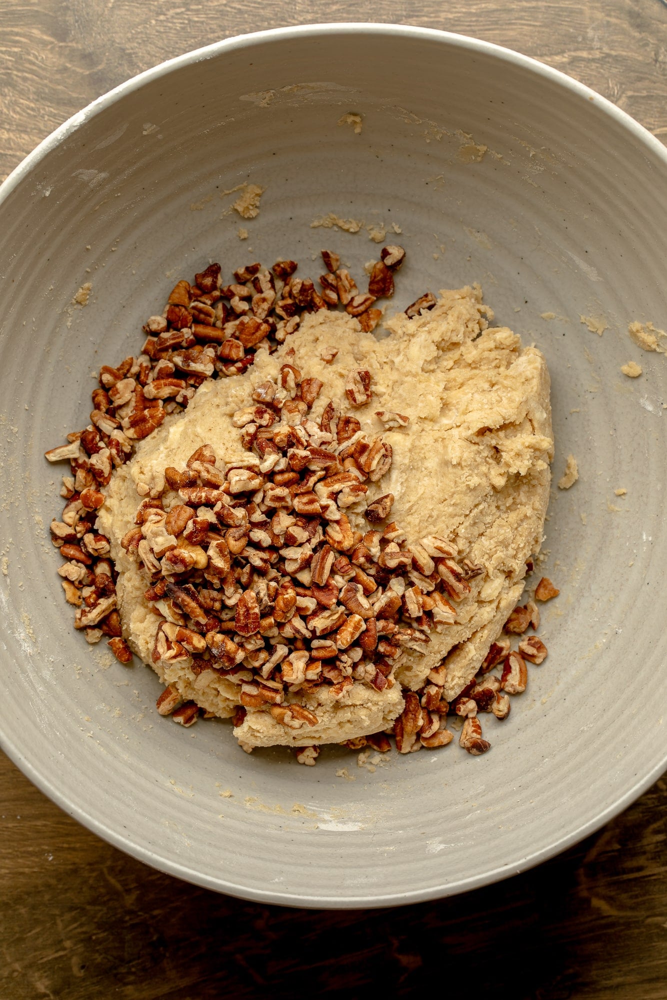 overhead view of a ball of maple pecan scone dough covered with chopped pecans in a large bowl.