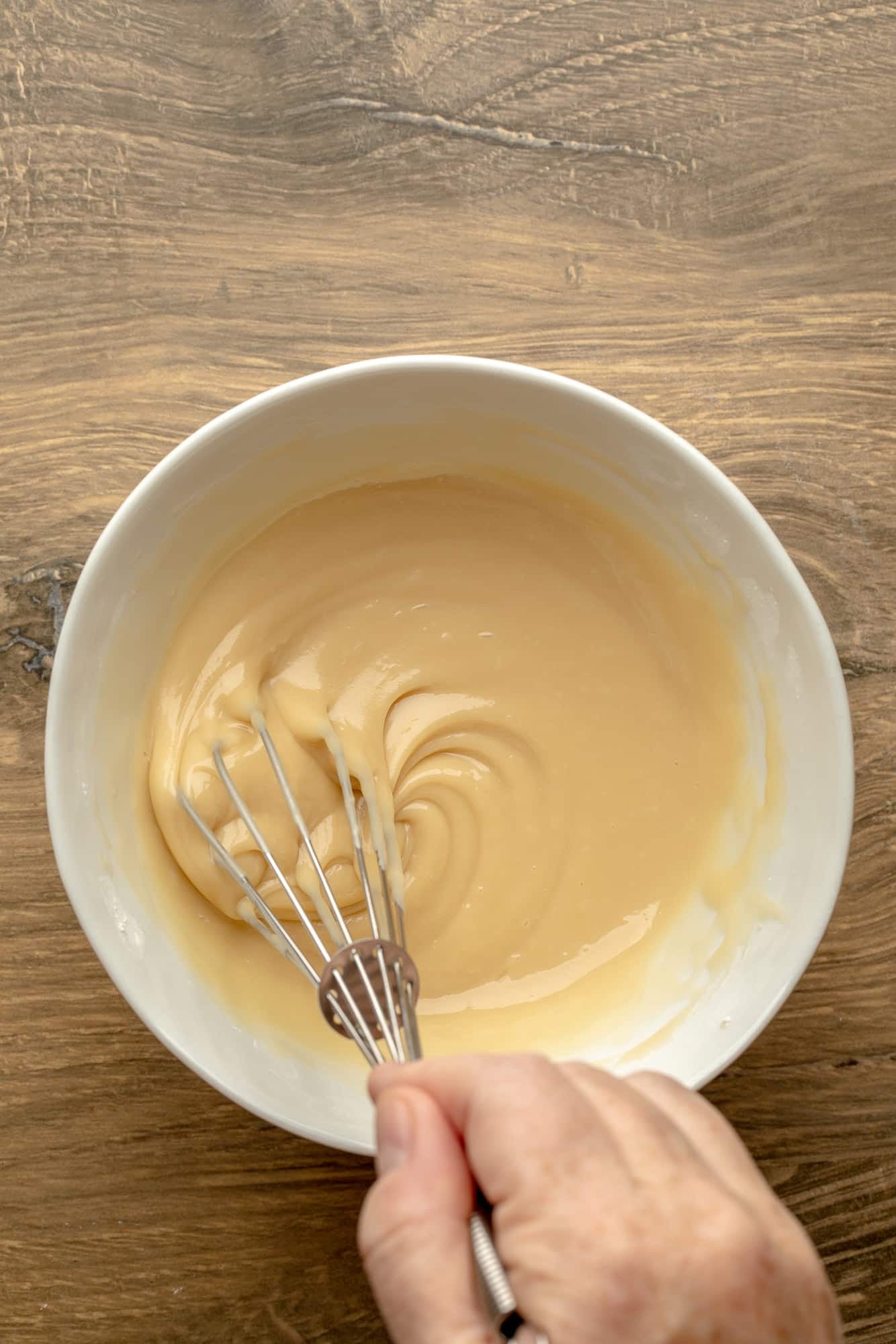 overhead view of a hand whisking maple glaze in a bowl.