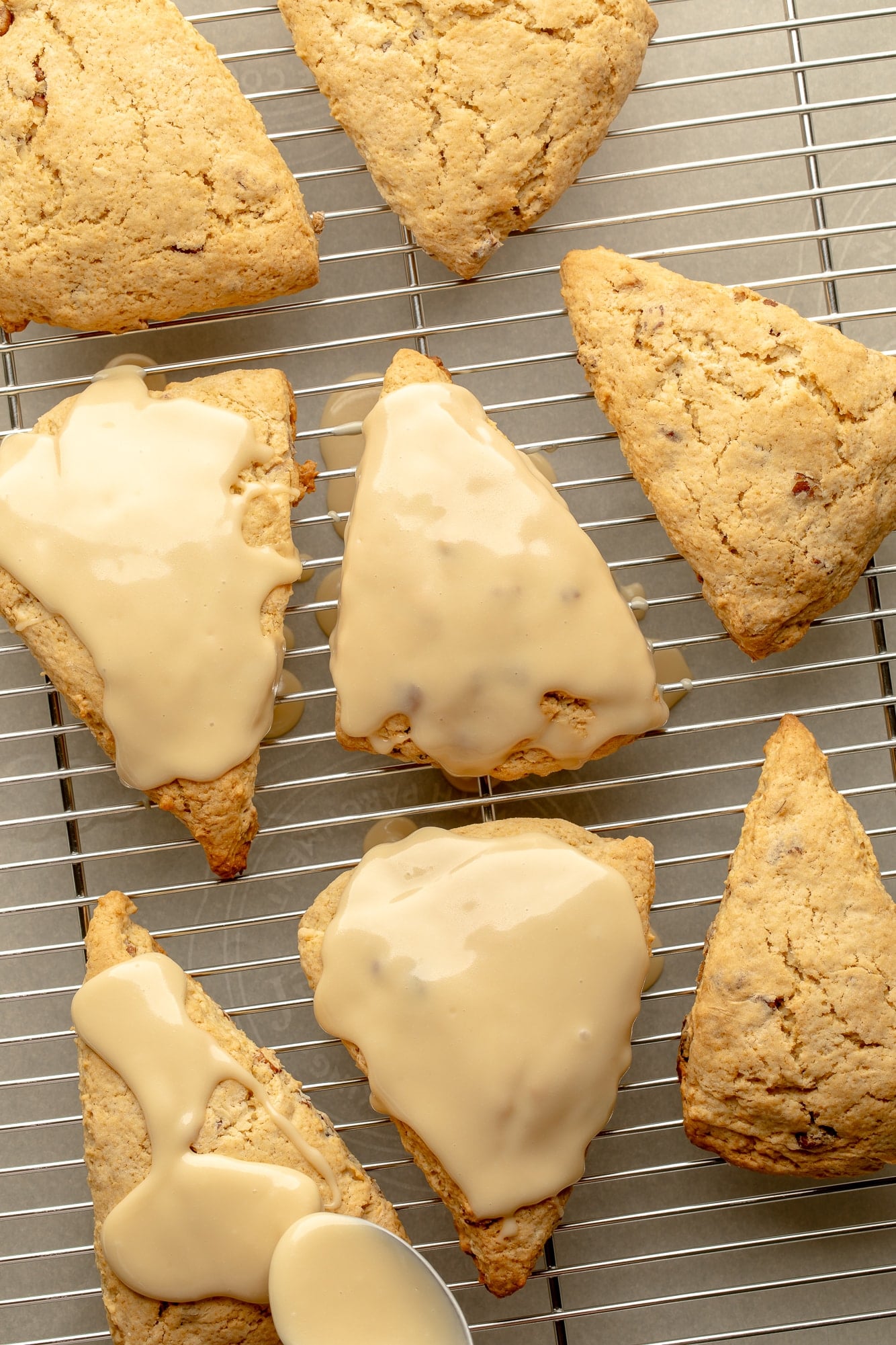 overhead view of baked maple pecan scones on a wire rack being topped with maple glaze.