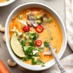 overhead view of a bowl of Thai Coconut Soup (Vegan Tom Kha) topped with fresh herbs and red chili peppers.