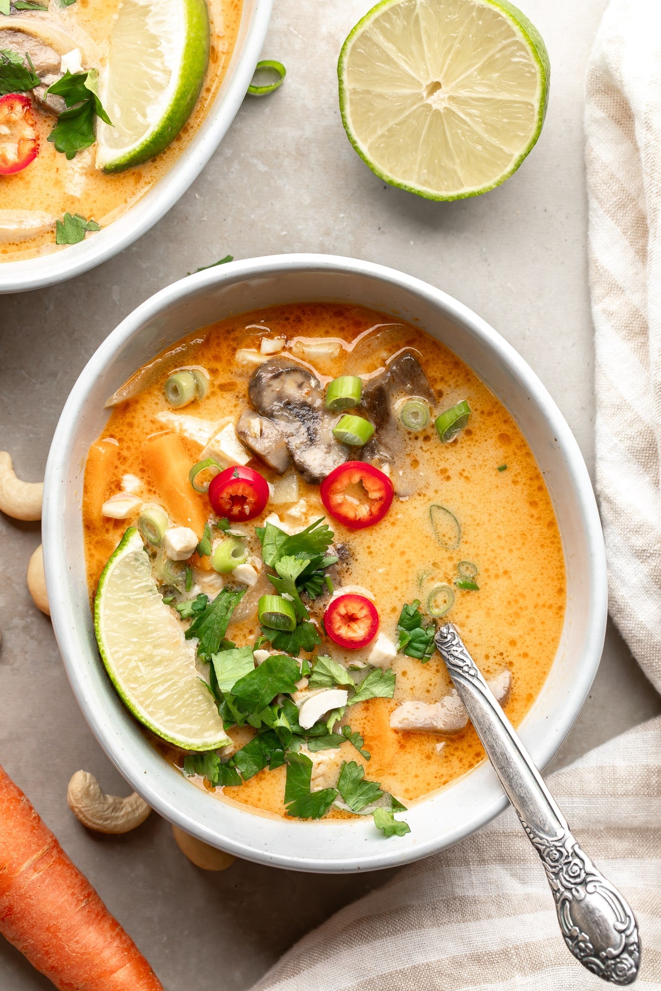 overhead view of a bowl of Thai Coconut Soup (Vegan Tom Kha) topped with fresh herbs and red chili peppers.