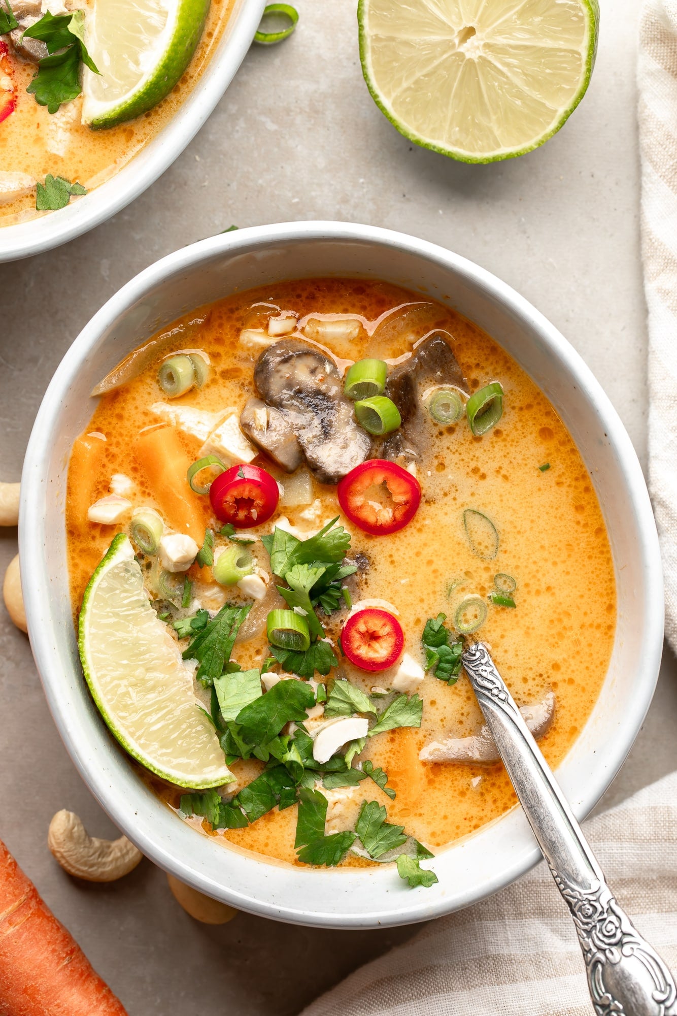 overhead view of a bowl of Thai Coconut Soup (Vegan Tom Kha) topped with fresh herbs and red chili peppers.