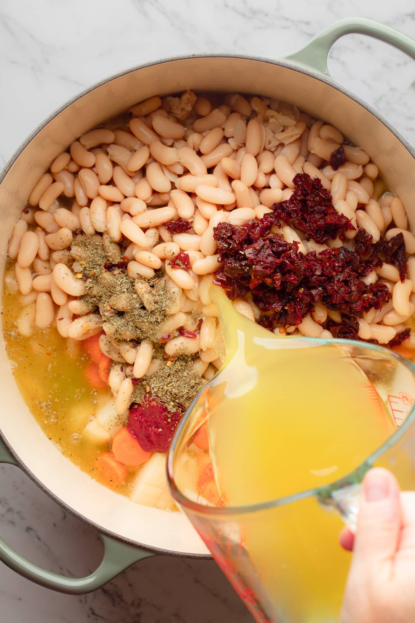 overhead view of broth being poured into a large pot filled with the ingredients for Tuscan white bean soup.