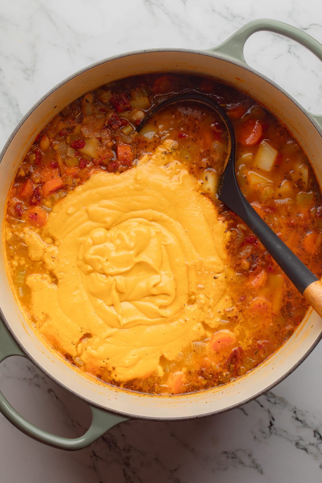 overhead view of a black ladle in a large pot of Tuscan white bean soup.