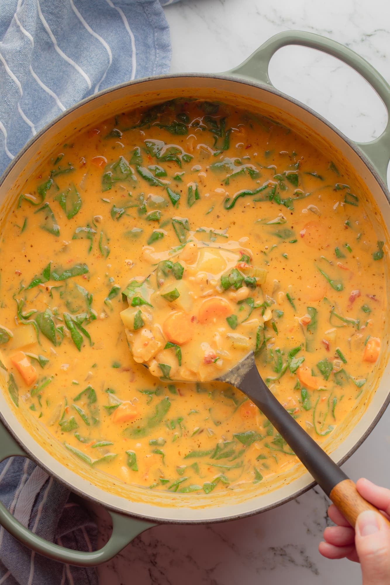overhead view of a hand lifting a ladle of Tuscan white bean soup from a large pot.