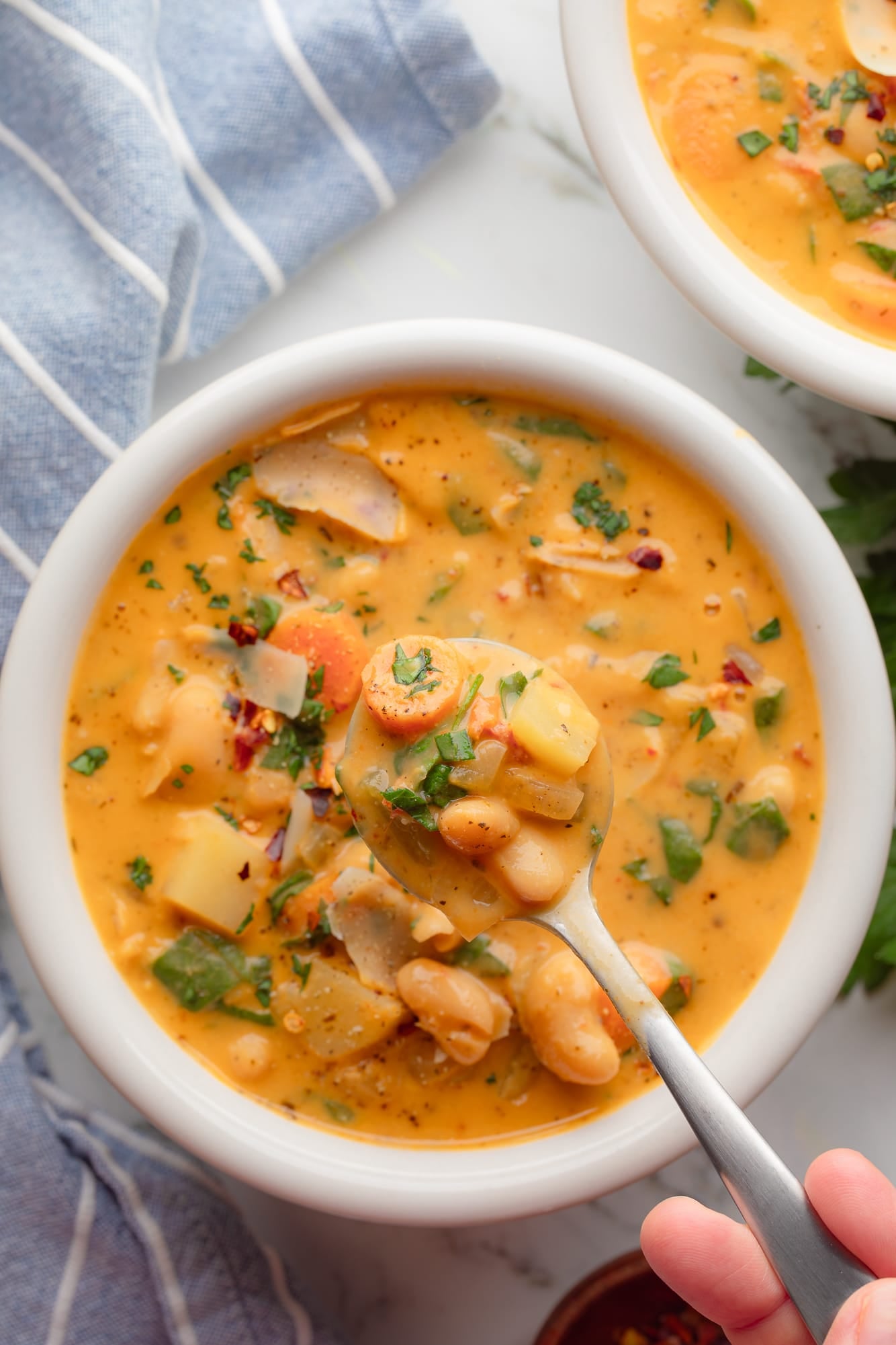 overhead view of a hand lifting a spoonful of Tuscan white bean soup from a bowl.